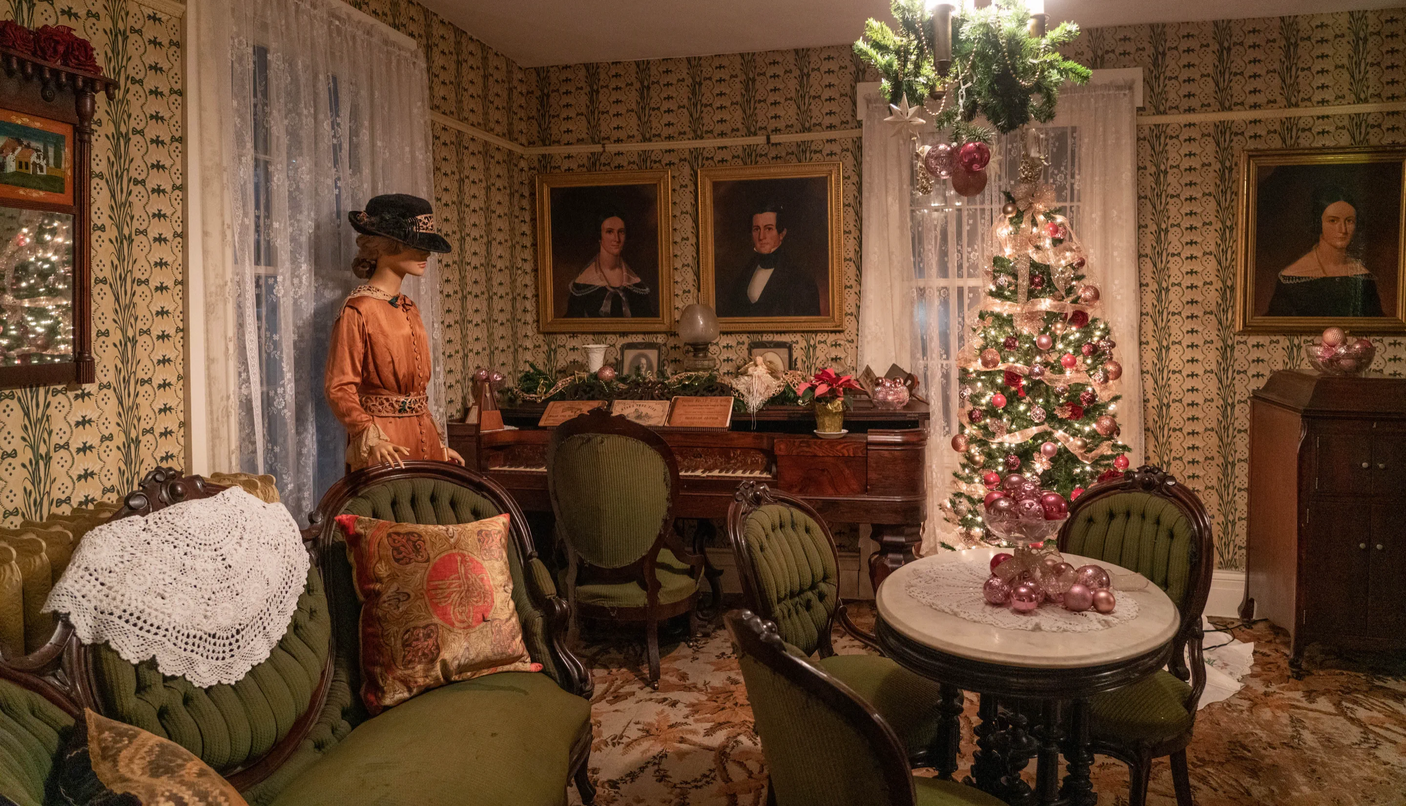 A Christmas tree glowing beside the piano in the decorated Boothe Homestead parlor