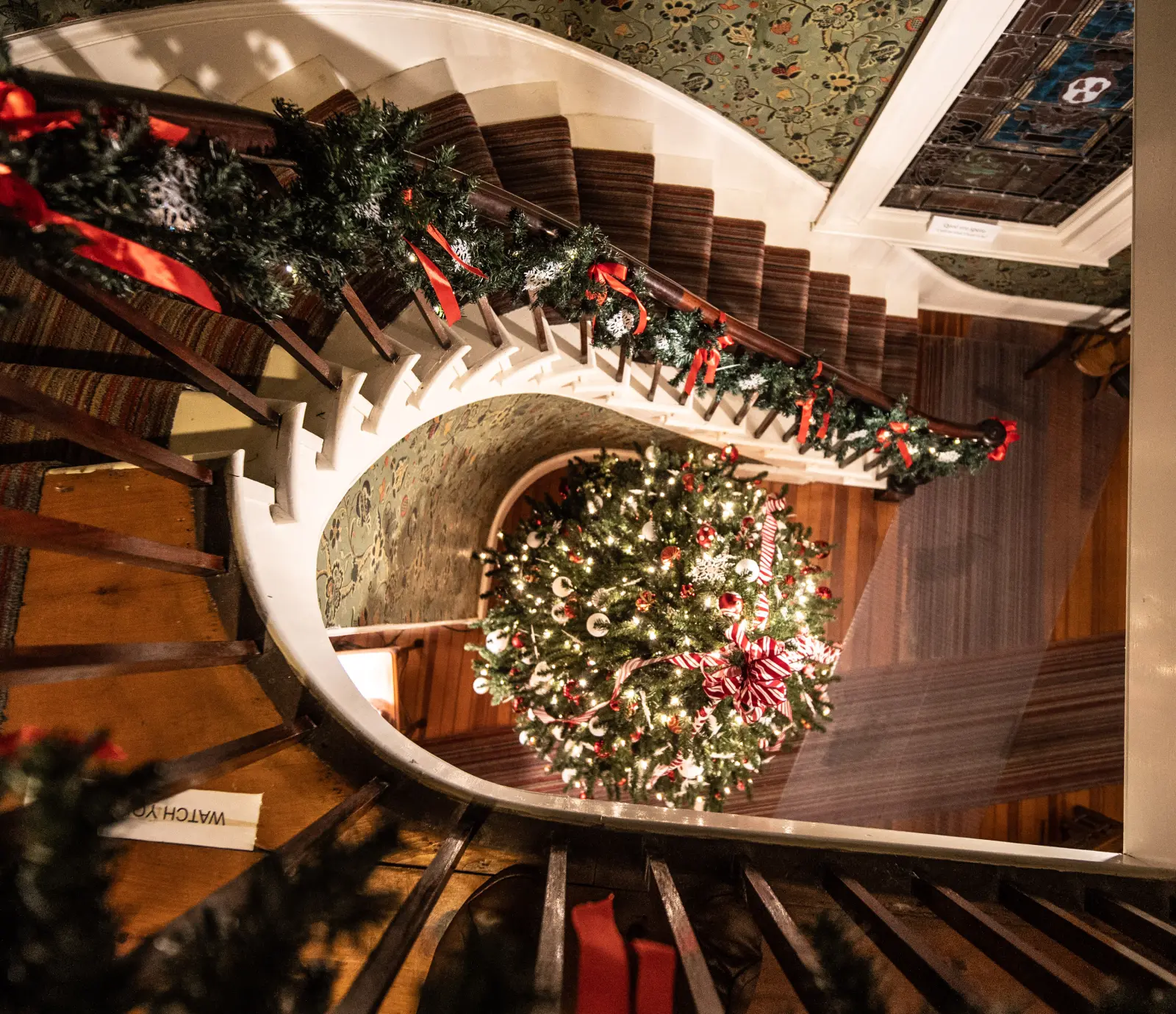 A Christmas tree and garland decorating the curved staircase inside the Boothe Homestead