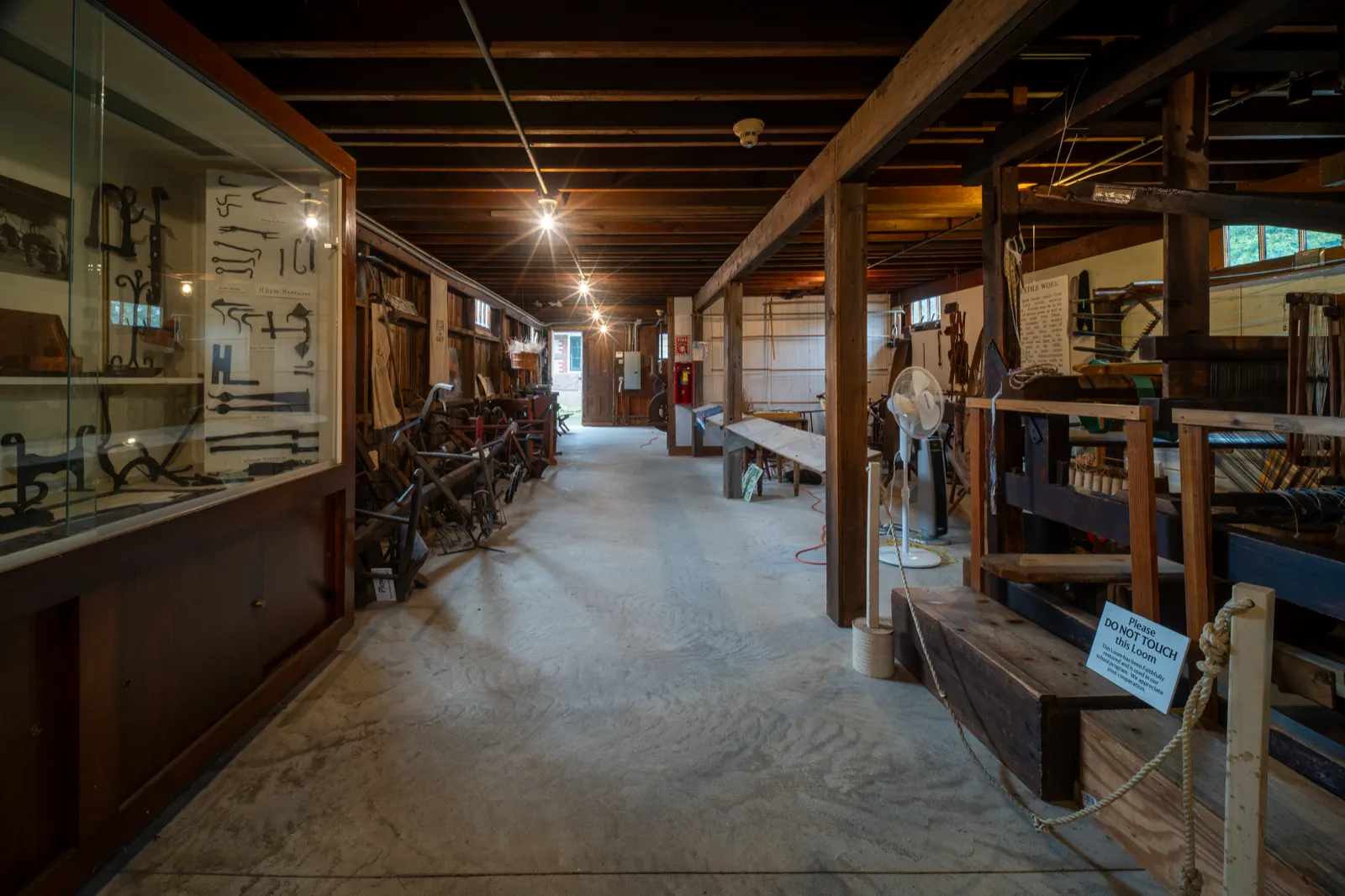 Long interior aisle of the Americana Museum lined with hand tools, farm equipment, and textile displays
