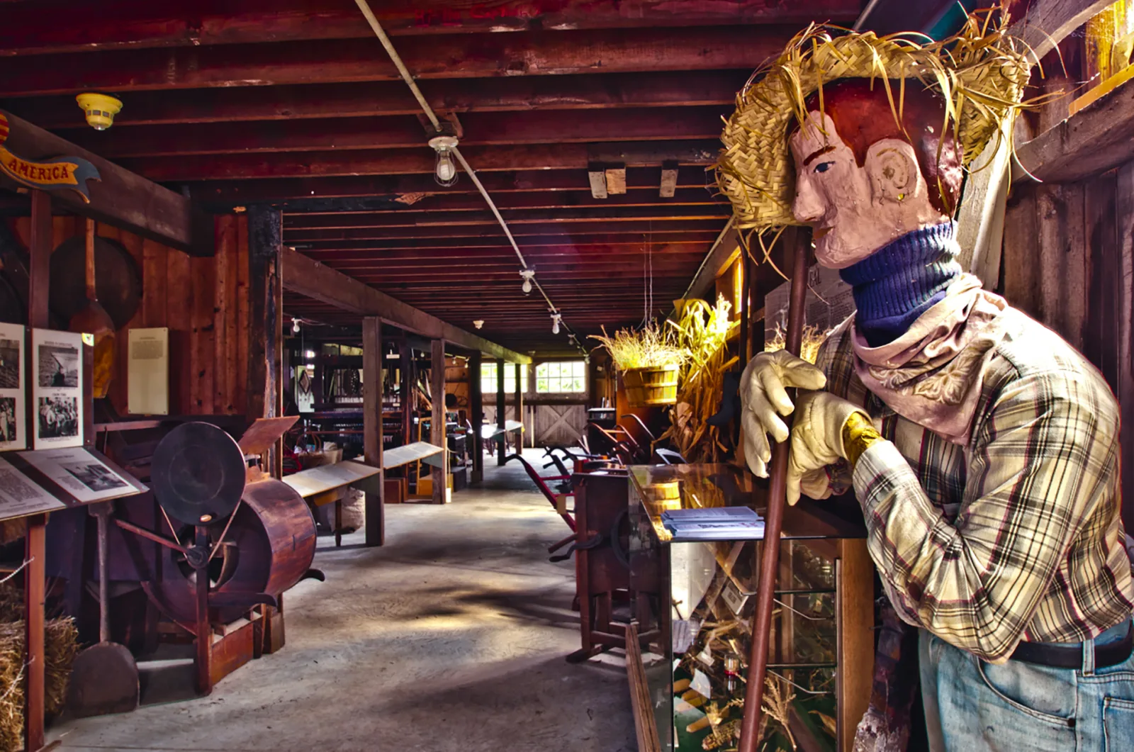 A scarecrow figure beside farm tools and exhibits inside the Americana Museum tool shed