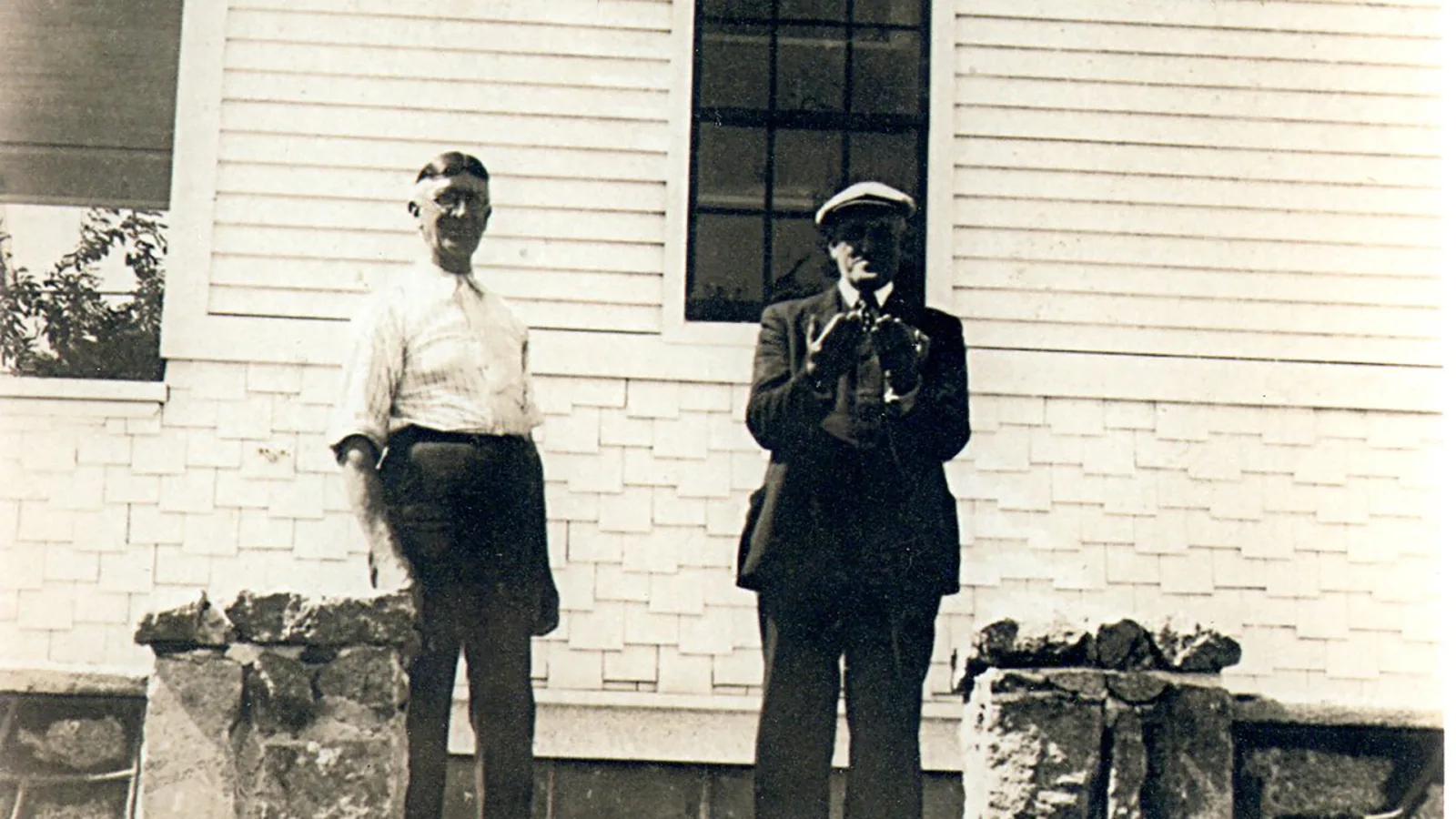 Two men standing between stone pillars outside a building on the Boothe property