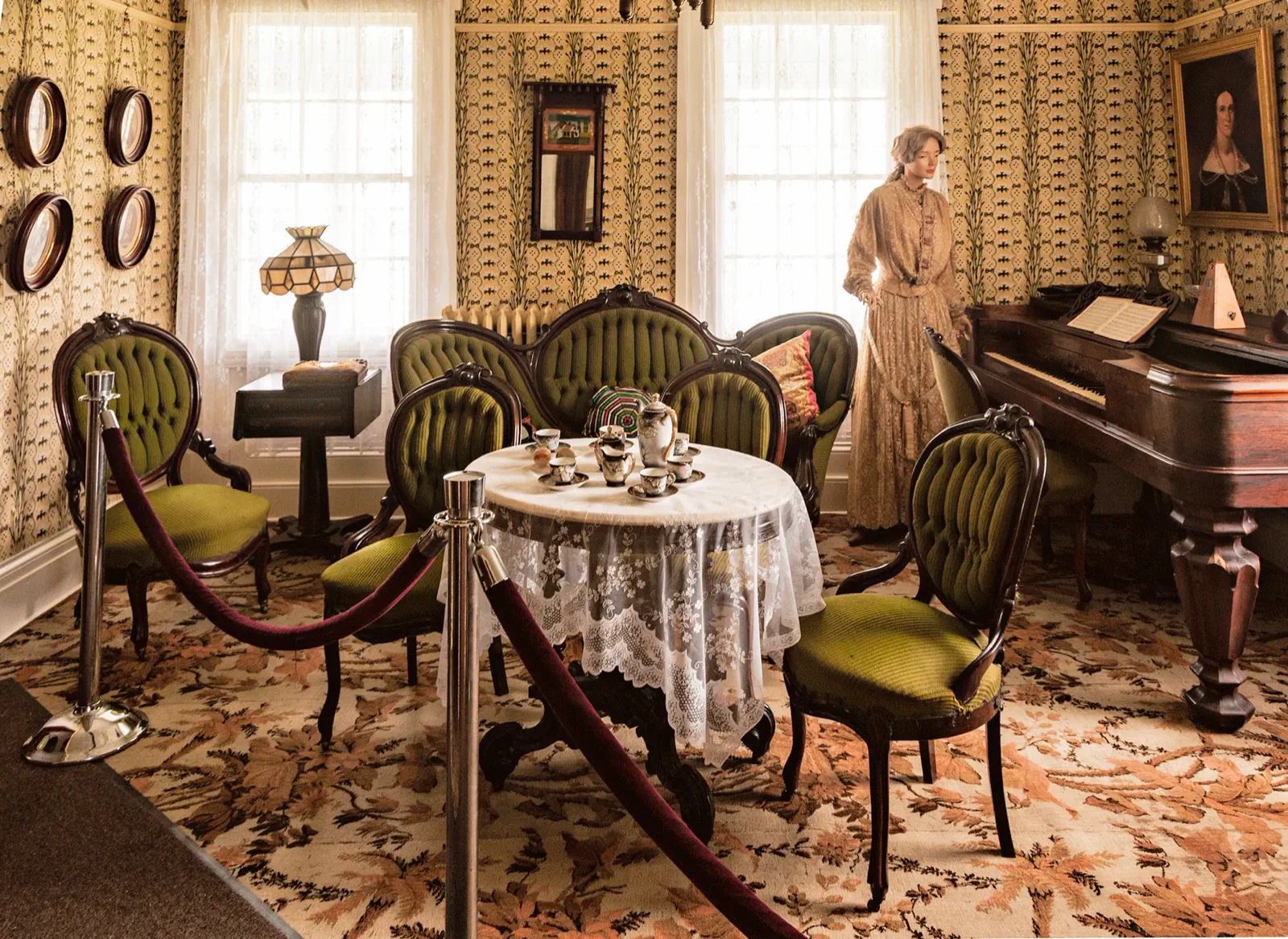 The Boothe Homestead parlor furnished with green seating, a tea table, piano, and period displays