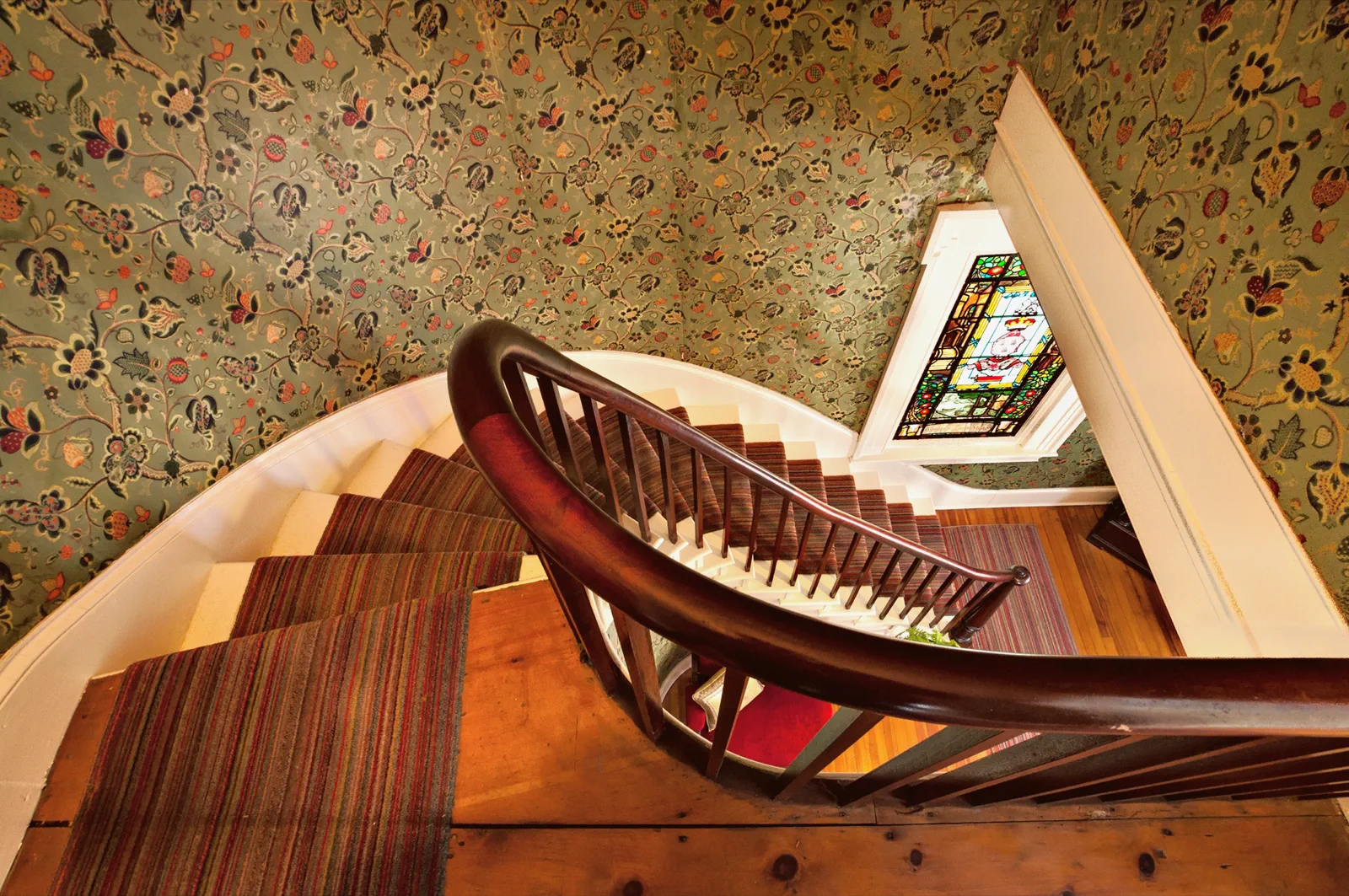 Curved wooden staircase and stained-glass window inside the Boothe Homestead