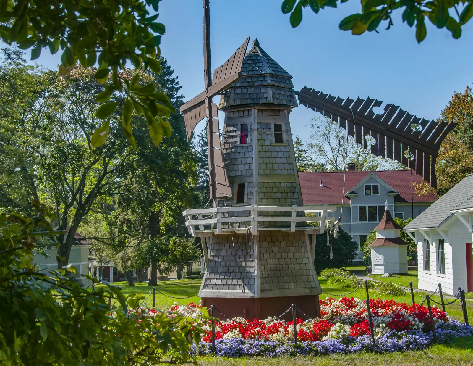 The Boothe Park miniature windmill framed by leafy branches and colorful flower beds