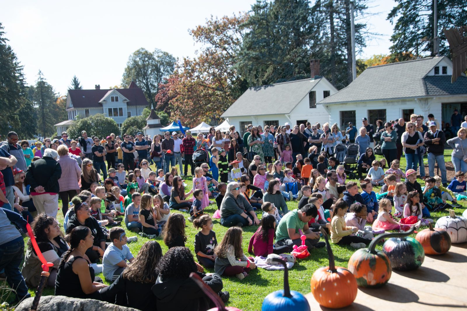 Families seated on the lawn watching a performance, with painted pumpkins lining the stage